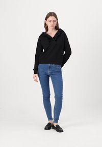 Melna kapuce ar V-veida kakla izgriezumu un drapētiem akcentiem, apvienota ar ziliem skinny džinsiem un melnām mokasīnām. Minimālisma dizains un auduma tekstūra.