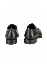 Zwarte leren schoenen met afgeronde neus, gladde textuur en een lage, stevige hiel. Voorzien van subtiele branding en een driekleurige accenten aan de achterkant.