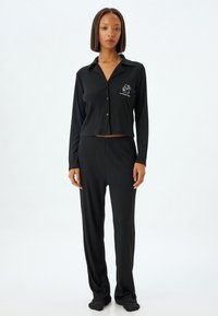 Conjunto de pijama negro que incluye una camisa de manga larga con botones, cuello y textura acanalada, combinada con pantalones sueltos a juego. Detalles bordados como acento.