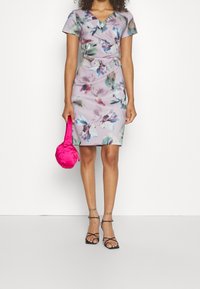 Blomsterprydd klänning i ljus lavendel med korta ärmar och en figurnära silhuett. I kombination med en rosa satinhandske och svarta sandaler med remmar.