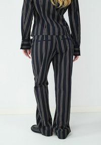 Zwarte gestreepte pak met een op maat gemaakt jasje en flared broeken. De stof heeft een gladde textuur met contrasterende dunne strepen in wit en beige.