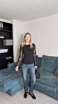 Čierny top s priesvitnými vyšívanými rukávmi, kombinovaný so svetlo modrými denimovými džínsy. Oblečenie dopĺňajú čierne mokasíny a kabelka.