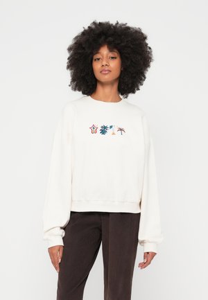 Kremfarget genser med løs passform, ribbestrikkede mansjetter og rund hals. Har et flerfarget brodert motiv av palmetrær og stjerner.