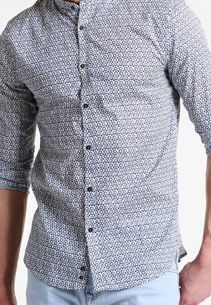 Chemise à boutons en tissu bleu clair avec un motif circulaire en bleu foncé et blanc, dotée d'un col évasé et de manches trois-quarts.