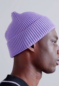 Berretto in maglia lavanda con righe verticali, cima arrotondata e texture morbida. Indossato da una persona di pelle scura, che mostra un profilo laterale.