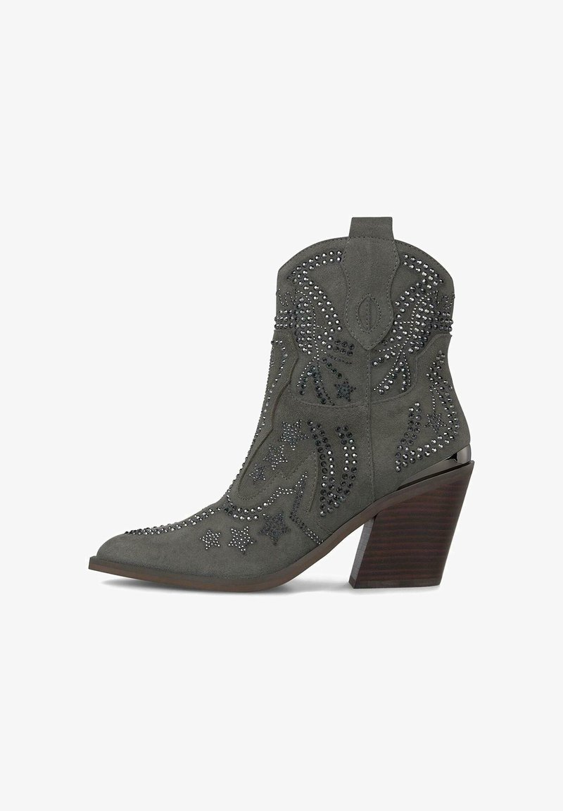 Bota de cowboy de ante gris con punta afilada, adornada con tachuelas plateadas en patrones de estrellas y flores, y un tacón de madera decorativo.