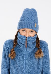 Giacca in pile blu con colletto alto e zip, abbinata a un cappello in maglia blu. Entrambi presentano un aspetto morbido e accogliente.
