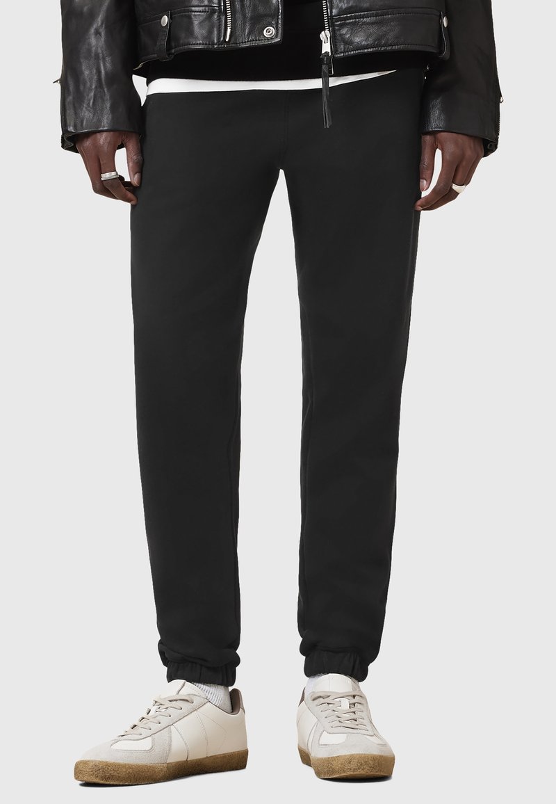 Svarta sweatpants med elastiska muddar, tillverkade av mjukt tyg. Bärs med vita sneakers med beige detaljer och strukturerade sulor.