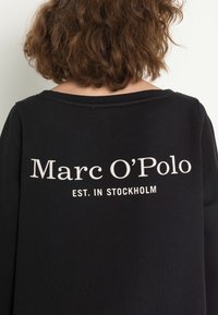 Svart sweatshirt med "Marc O'Polo" och "EST. IN STOCKHOLM" tryckt i vitt på baksidan. Mjuk tyg med bred halsringning.