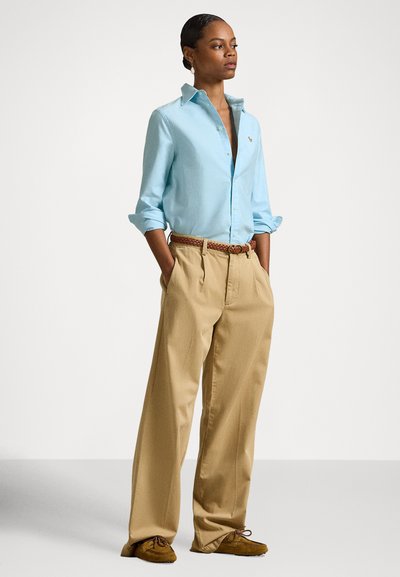 Gaiši zila pogām apvilkta krekls, khaki platu kāju bikses un brūnas mokasīnu stila kurpes ar austu jostu ar teksturētu dizainu.