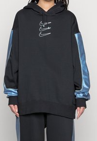 Svart hoodie med dragkedja och blåa satinsidopaneler samt Nike-logotyp i mitten. Har en justerbar huva och ribbade ärmslut.