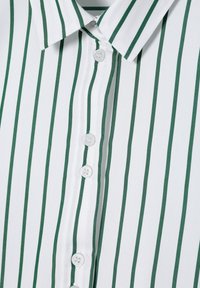 Chemise blanche à rayures verticales vertes, avec un col pointu et des boutons blancs sur le devant.
