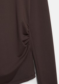 Ciemnobrązowa bluzka z długim rękawem, wykonana z miękkiego materiału. Posiada marszczone detale po bokach oraz prosty dół z minimalnym szyciem.