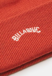 Pletena narančasta kapa s rebrastom teksturom. Ima bijeli izvezeni "Billabong" logo u lučnom dizajnu sprijeda.