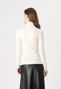 Pull à col roulé beige clair avec des manches longues, fabriqué en tissu doux. Présente un design ajusté et des poignets côtelés, assorti à une jupe en cuir noir.