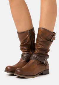 Bottes montantes en simili cuir marron avec un design relâché, fermeture éclair et une sangle décorative à boucle avec des clous. Fini texturé.