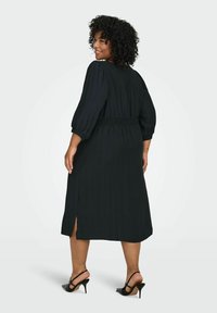 Melnas midi kleitas ar teksturētu audumu, savilktu jostasvietu un pūstām piedurknēm. Ar sānu šķēlumiem un saderīgas melnās augstpapēžu kurpes.