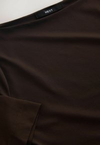 Brown, short-sleeve top made of smooth fabric. Features a round neckline and minimal stitching details. Brand label "NEXT" visible.