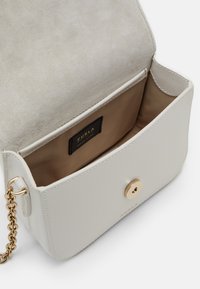 Vit läder crossbody-väska med guldknapplås, kedjerem och beige insidan med en liten märkesetikett.
