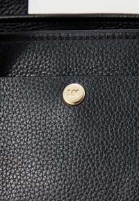 Portafoglio in pelle nera con superficie strutturata, decorato con un bottone logo di colore oro bronzato, embossato con "MK".
