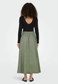 Haut noir à manches longues et jupe longueur genou vert olive à taille élastique, texture lisse et design fluide. Sandales noires.