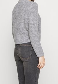 Pull gris en tricot avec une finition texturée, col arrondi et manches longues, associé à un jean en denim foncé avec poches arrière.