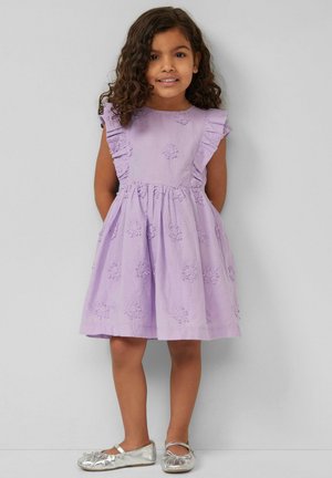 Young girl with curly hair wearing a lavender dress with floral embroidery and ruffled sleeves, paired with silver Mary Jane shoes.