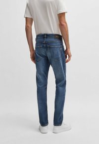 Mörkblå jeans i rak skärning, fem fickor och ett svart logoband. Kompletterad med vita sneakers.