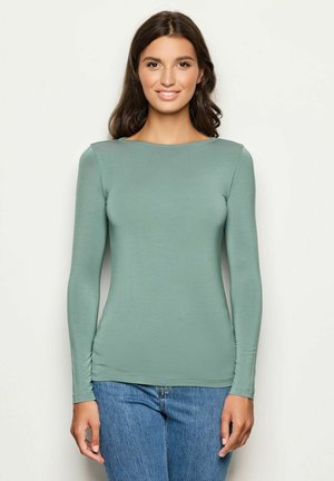 Haut à manches longues en tissu vert doux, coupe ajustée, encolure ronde, texture lisse, associé à un jean bleu décontracté.