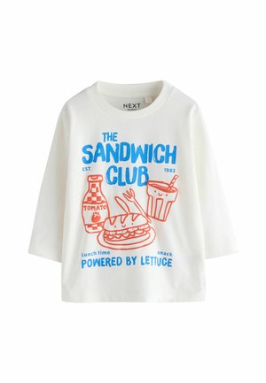Hvid langærmet skjorte med blå og rød print af en sandwich, flaske tomatsovs, drik med sugerør og tekst om sandwichklubben.