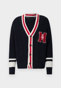 Μπλε ναυτικό πλεκτή ζακέτα με V-λαιμόκοψη, ρίγες κόκκινου και άσπρου στο τελείωμα, κούμπωμα με κουμπιά και κεντημένο γράμμα "H" στο στήθος.