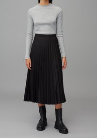 Grauer Langarmoberteil mit Rippstruktur, kombiniert mit einem schwarzen, plissierten Midirock. Schwarze Stiefeletten runden das Outfit ab.