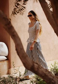 Haut peplum à pois noir et blanc avec des bretelles en forme de nœud, associé à un pantalon large rayé noir et blanc ; les chaussures sont noires.