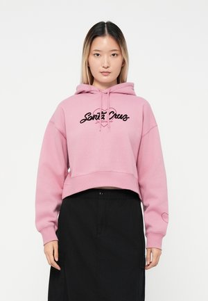 Hoodie cropped rosa con logo ricamato "Santa Cruz" in nero. Presenta un cappuccio con cordino e polsini a coste. Indossato con una gonna nera.