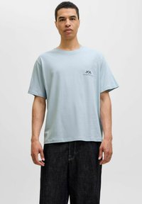 Lys blå kortærmet T-shirt lavet af blødt stof, med et lille sort grafisk motiv på venstre bryst og en afslappet pasform.