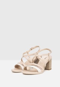 Sandali con tacco beige con cinturini incrociati, caratterizzati da una finitura in pelle liscia, una banda accentata bianca e un tacco a blocco texturizzato.