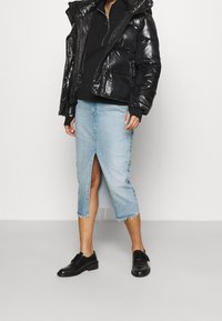 Svart glänsande pufferjacka med huva, svart sweatshirt under, ljusblå denimkjol med slits fram, och svarta snörskor.