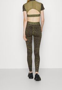 Conjunto de ropa activa en verde oliva que incluye una camiseta ajustada con espalda cortada y leggings de tiro alto con un patrón de leopardo.
