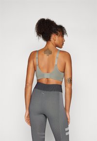 Sutiã desportivo em verde suave, com alças finas ajustáveis e faixa larga nas costas. Combinado com leggings pretas texturizadas de cintura alta.