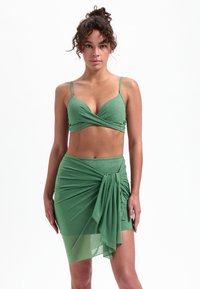 Zielony dwuczęściowy zestaw składający się z teksturowanego topu z krótkim rękawem w stylu owijanym oraz dopasowanej spódnicy z detalem w postaci wiązania i przezroczystą nakładką.