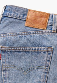 Zone de la poche arrière d'un jean en denim Levi Strauss bleu clair avec patch logo en cuir marron et étiquette de marque en tissu rouge.