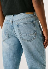 Světle modré džíny s volným střihem, s dvojitými zadními kapsami a hnědou koženou značkou na pasu.