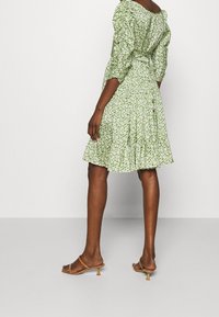 Green floral dress with puff sleeves, ruffled hem, and fitted waist. Light fabric features small white flowers against a green background.