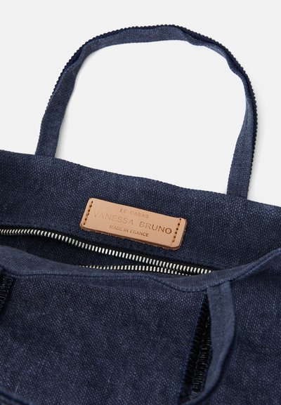 Sac fourre-tout en toile bleu marine avec label en cuir, fermeture éclair, et tissu texturé avec des poignées robustes. Vue intérieure.