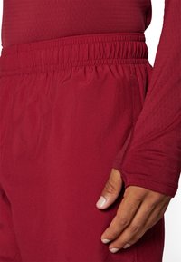 Pantalones deportivos burdeos con cintura elástica, tejido texturizado y costuras sin costuras, mostrados junto a una camiseta ajustada de manga larga.