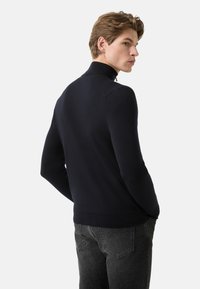 Marineblauer Pullover mit hohem Kragen, figurbetontem Schnitt, geripptem Saum und weicher Textur, kombiniert mit dunklen Denim-Jeans.
