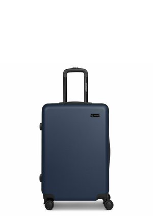 Valise rigide bleue avec quatre roues et une poignée télescopique noire déployée, posée verticalement sur un fond blanc.