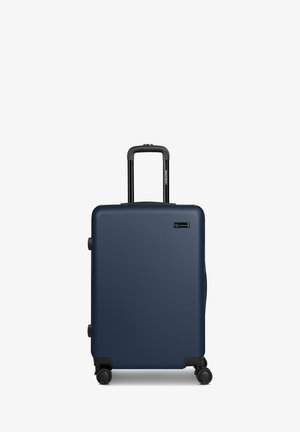 Maleta rígida azul con cuatro ruedas y un asa telescópica negra extendida, de pie sobre un fondo blanco.