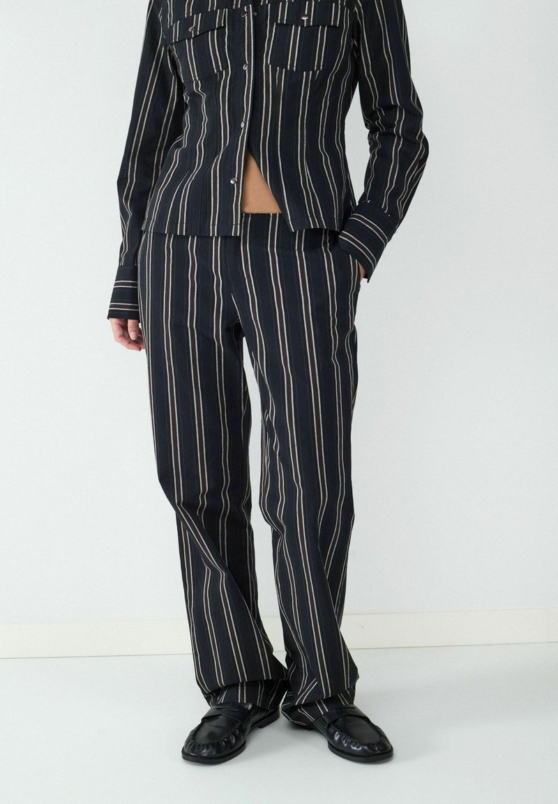 Zwart-wit gestreept tweedelig outfit bestaande uit een overhemd met kraag en bijpassende broek, gemaakt van een gladde, lichte stof.