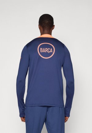 Long-sleeve athletic shirt in navy with orange accents. Features a circular "BARÇA" logo on the back. Smooth, moisture-wicking fabric.